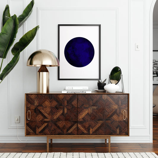 Blue planet minimalist graphic art print above a wood sideboard in an elegant space.