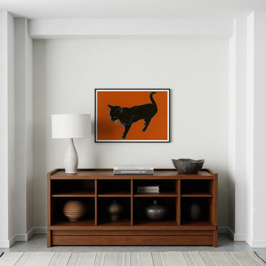 Art print with a black cat on an orange background in a bright interior.