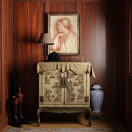 Framed fine art print depicting a sanguine portrait of a lady, in a dark interior with antique decorative cabinet with patterned cover, lamp, and porcelain Chinese vase against a wooden wall.