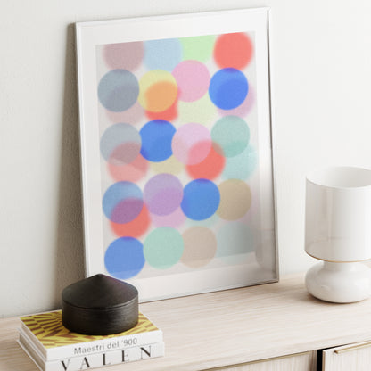 Framed abstract art with colorful circles on a shelf with books and a lamp.