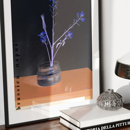 Framed art print of a glass vase with blue flowers on a wooden surface.