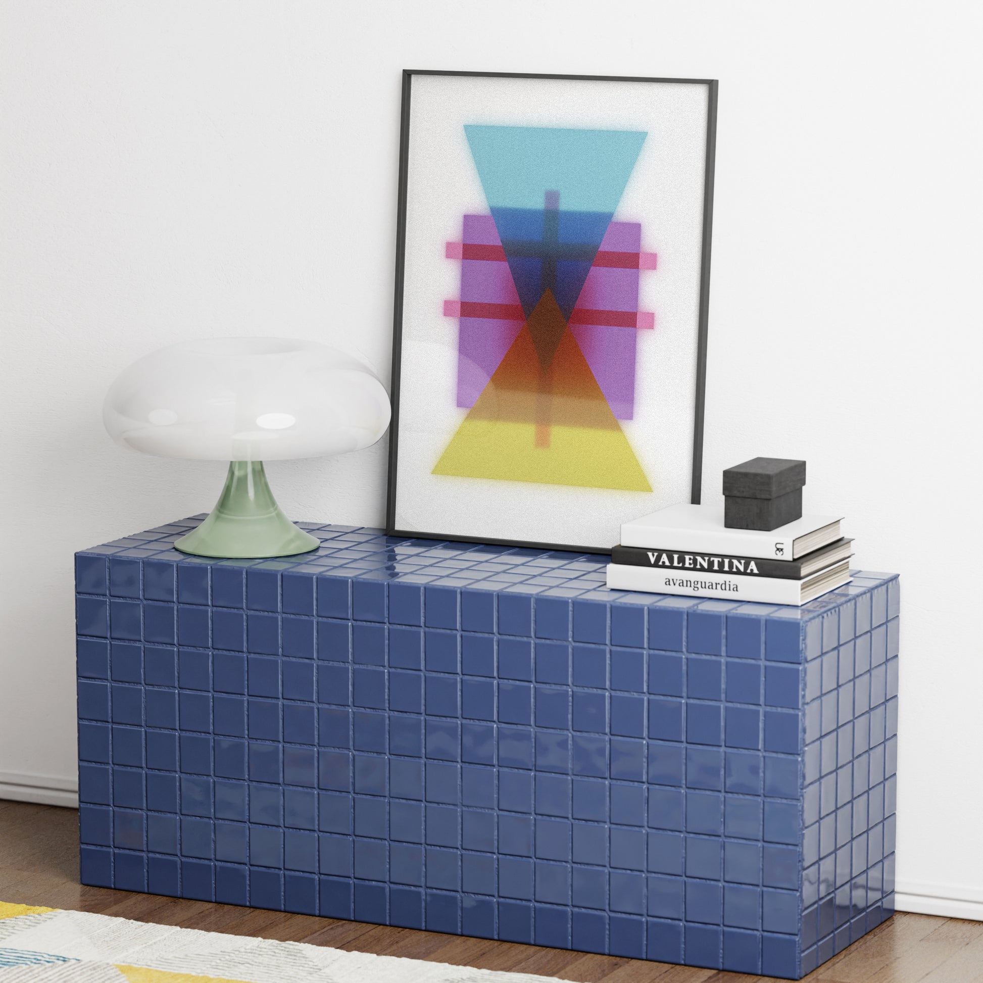 Blue tiled side table with a colorful abstract painting and books on top against a white wall.