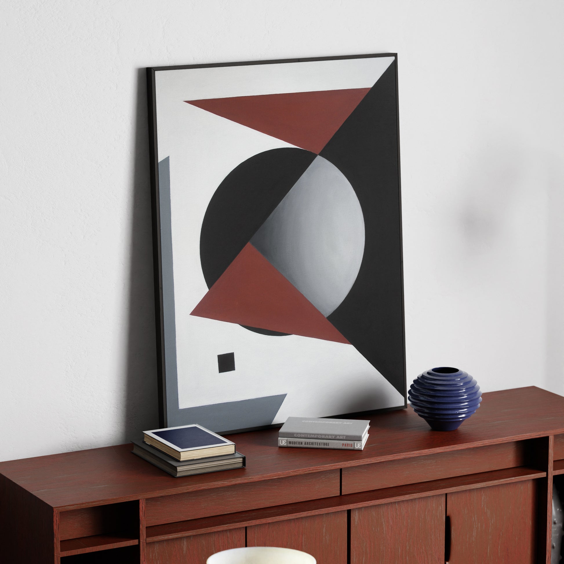 Suprematism painting with red, black and white on a red wood sideboard.
