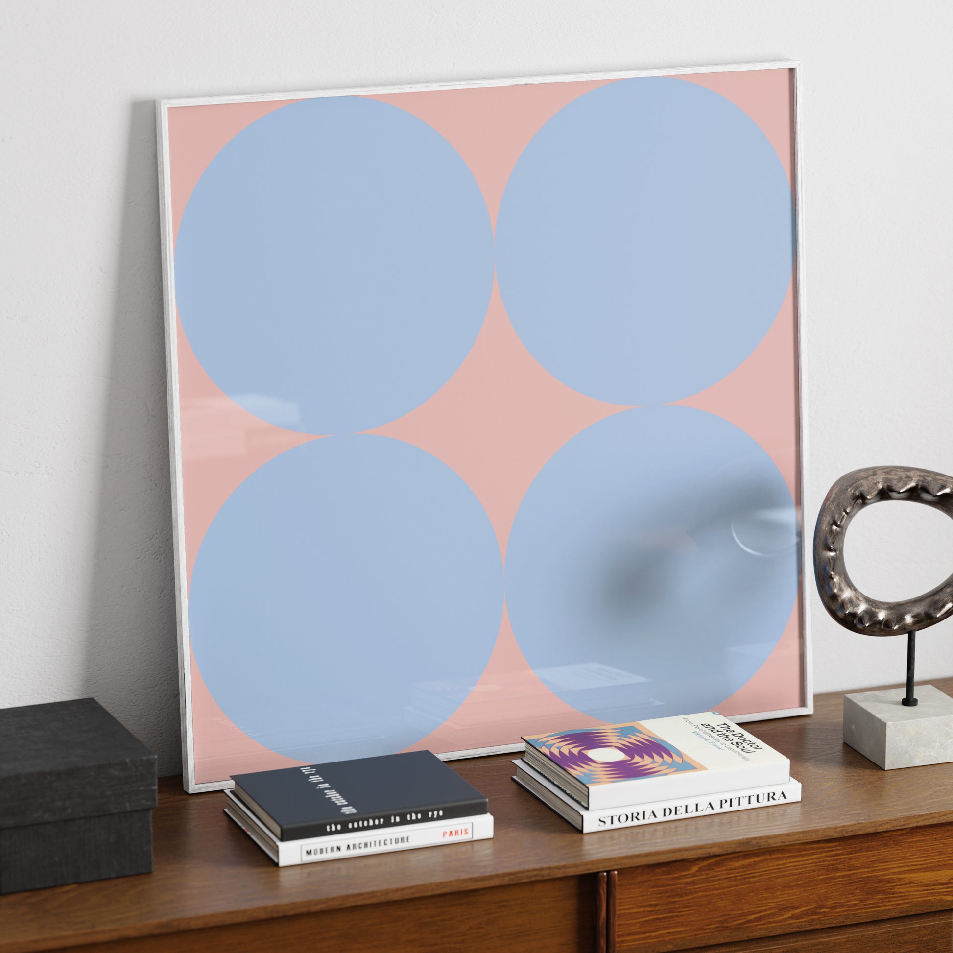 Contemporary minimalist art print with blue circles on pink, on a sideboard.