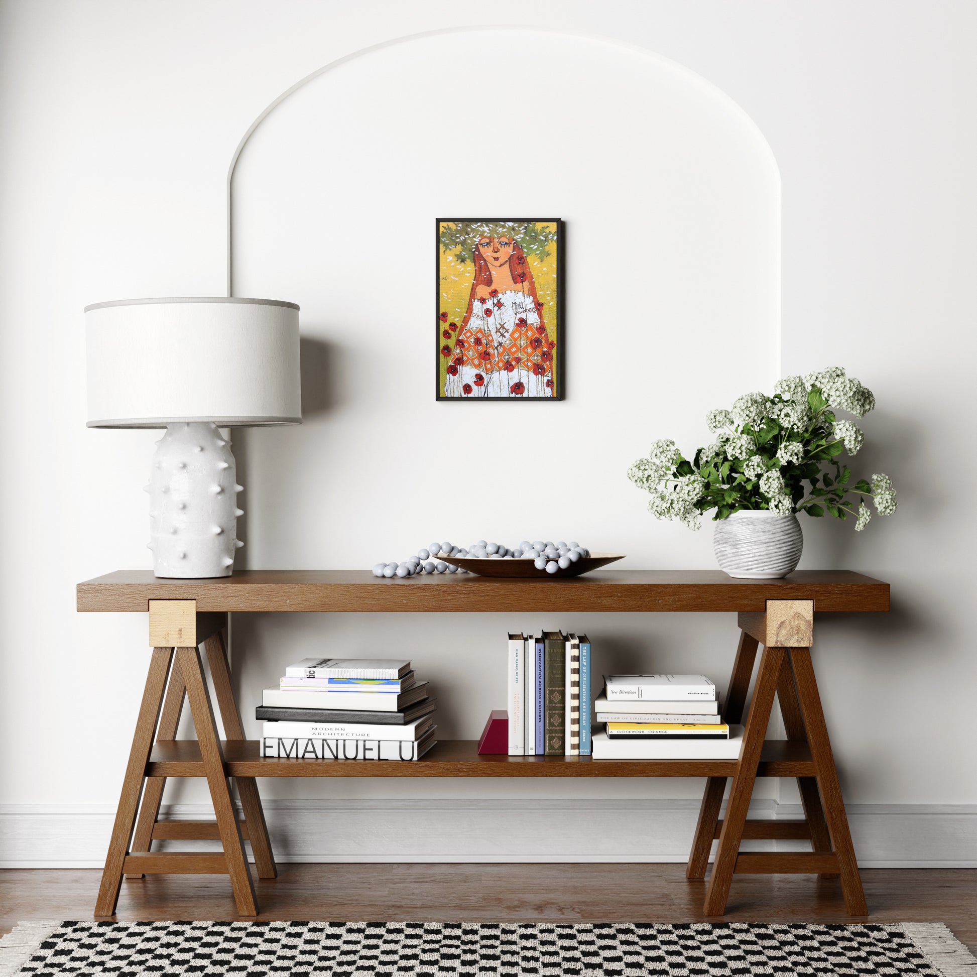 Wooden console table with books, a lamp, and flowers against a white wall.