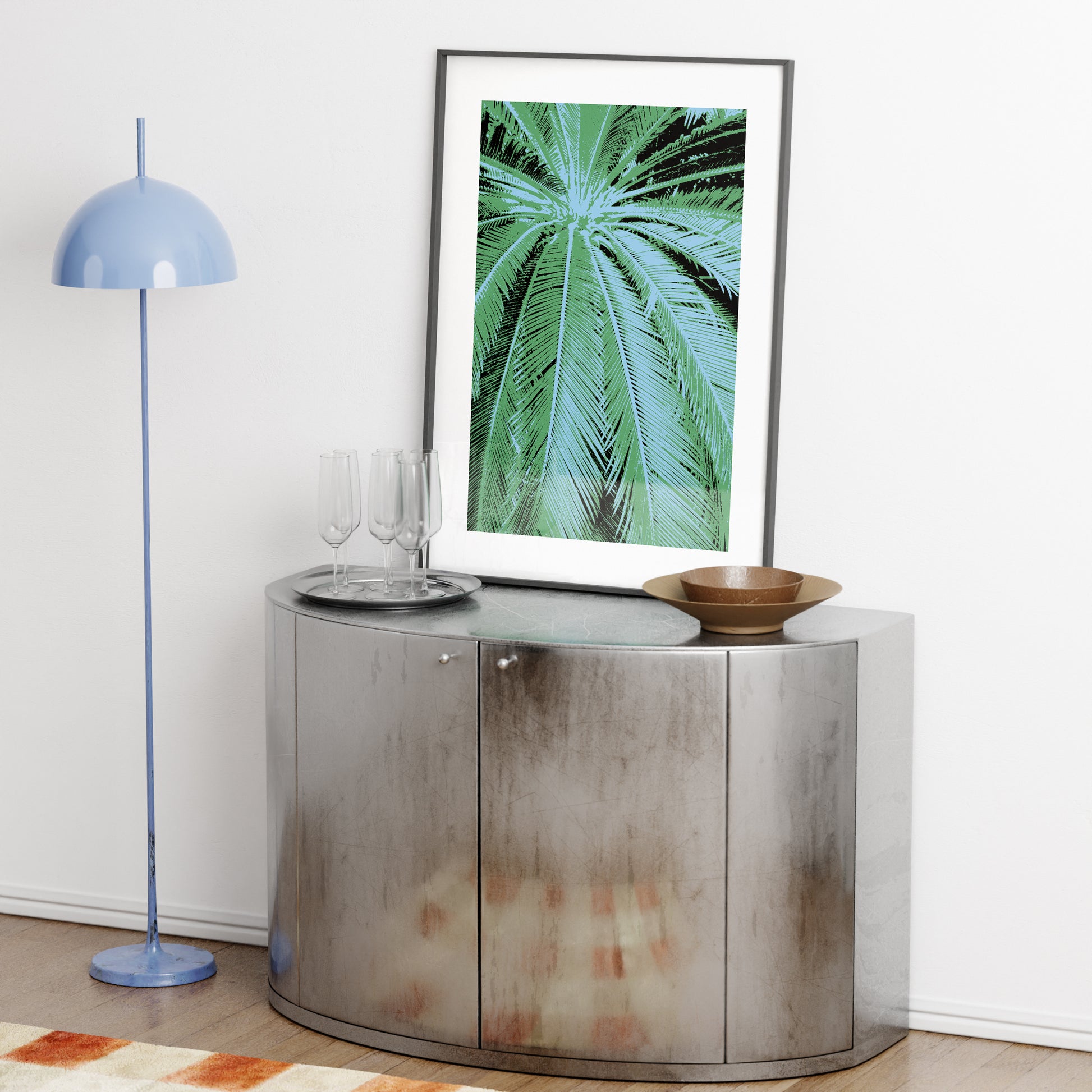Modern interior with a metallic console table, blue floor lamp, and framed artwork of a palm leaf.