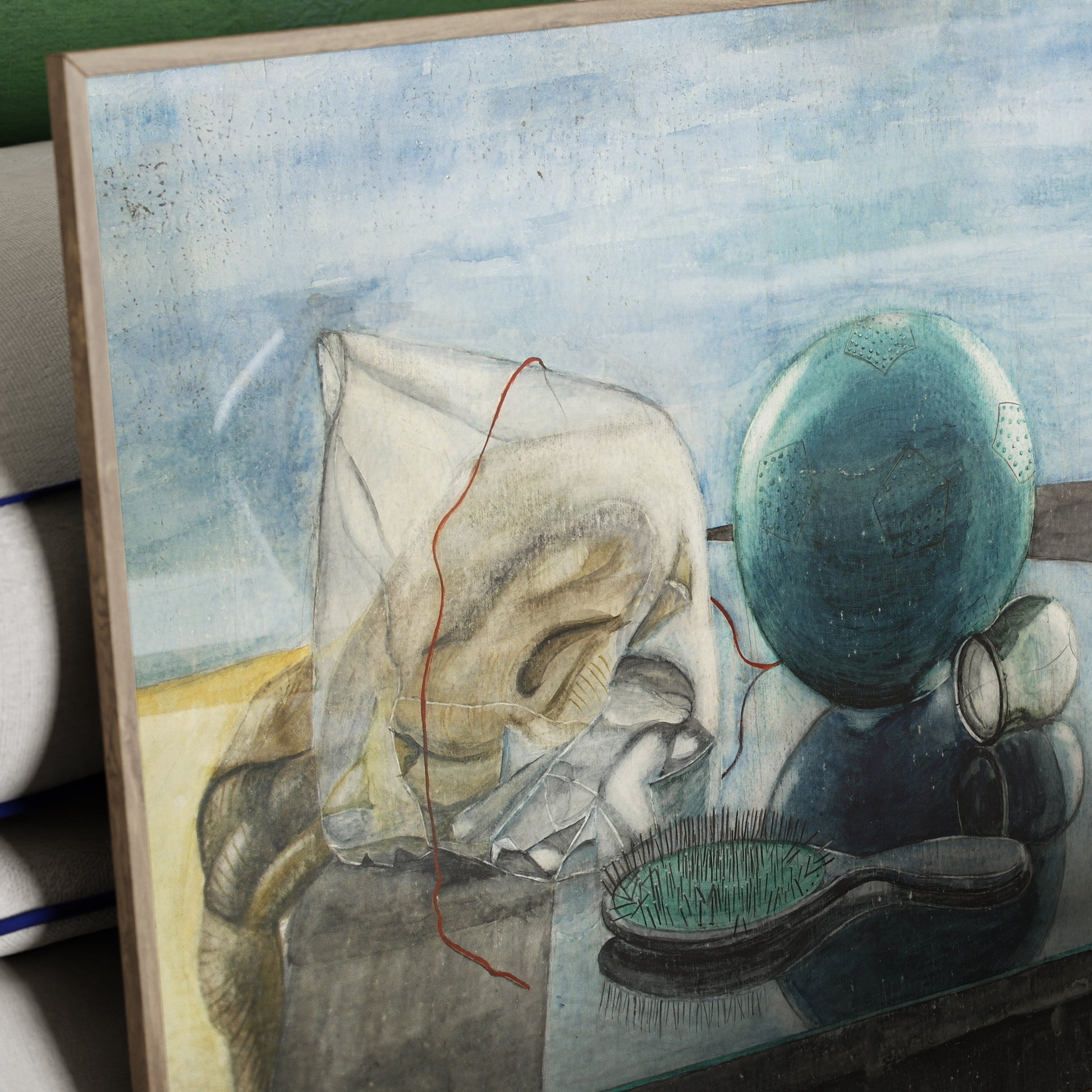 Detail of a framed figurative art print with blue-green ball, brush and various other objects, with a light blue sky on the background.