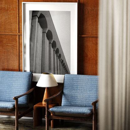 Two blue chairs with a lamp and framed picture on a wooden wall.