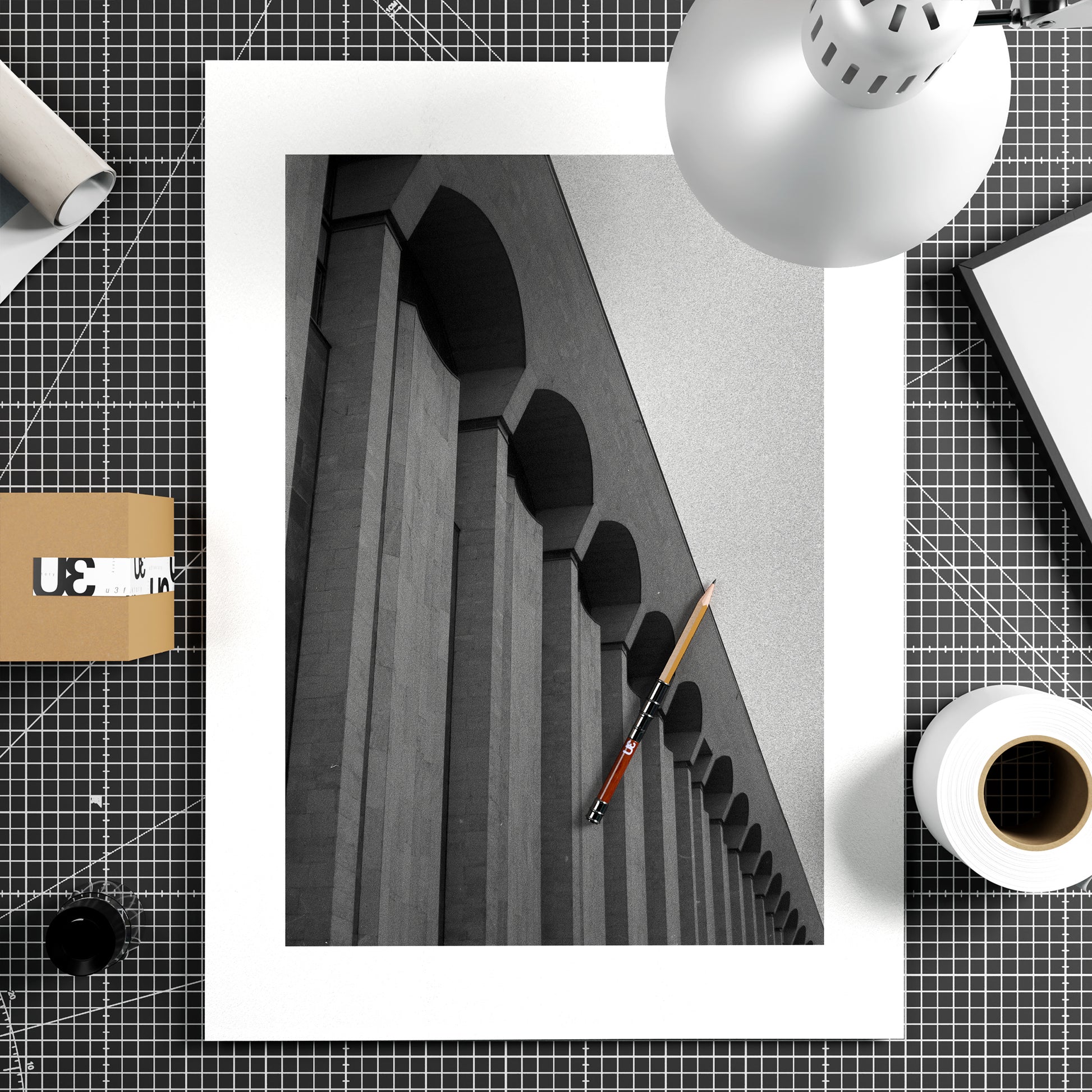 Framed black and white architectural photo on a grid-patterned surface with a pen and other objects.