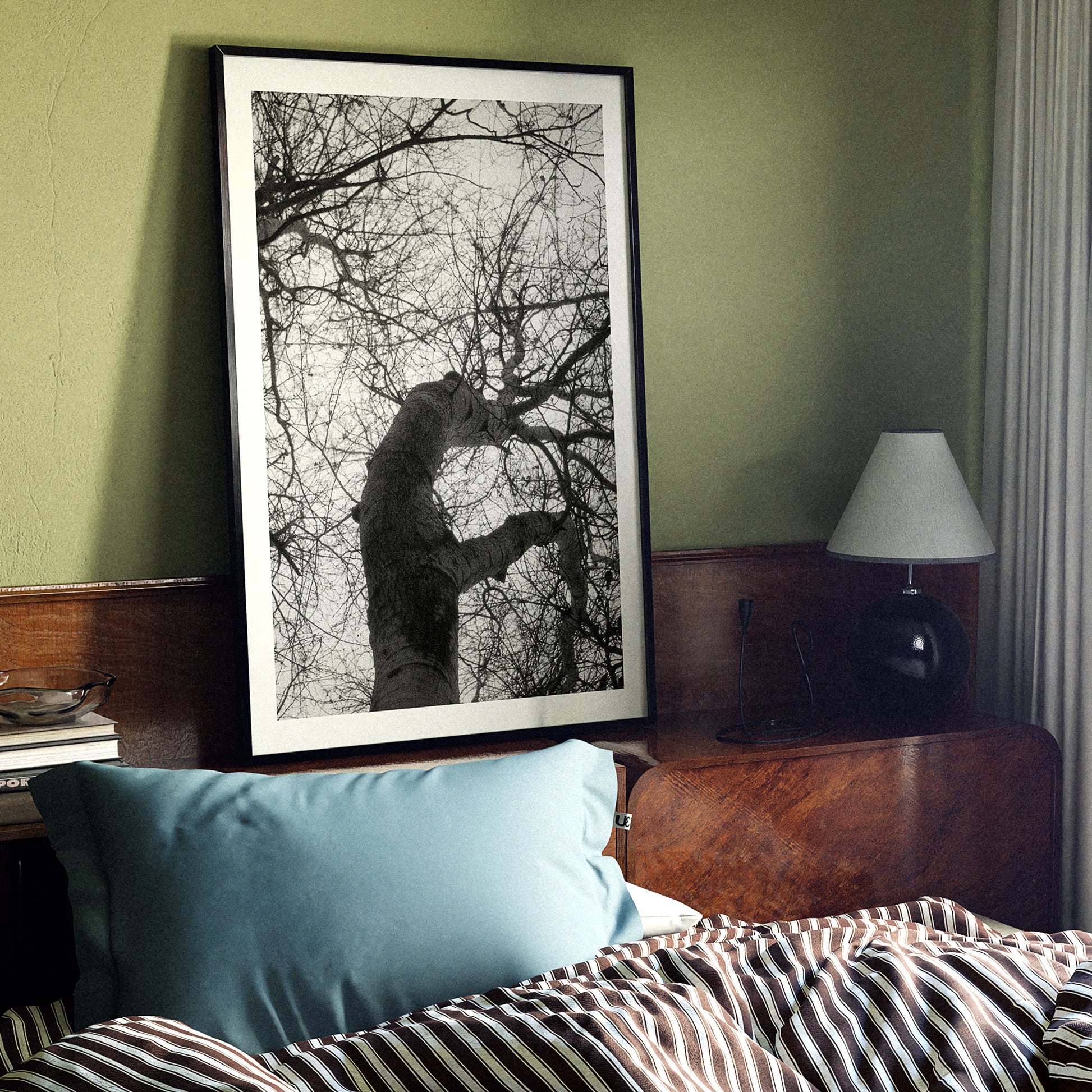 Framed black and white artwork above a bed with striped bedding and a blue pillow.