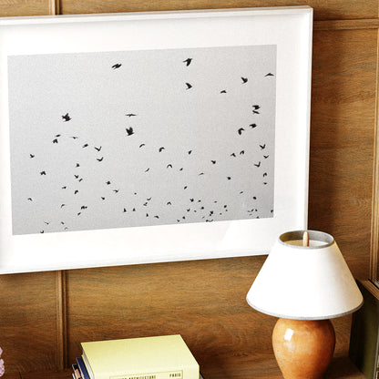 Framed artwork with black birds on a white background, placed on a wooden surface next to a lamp.