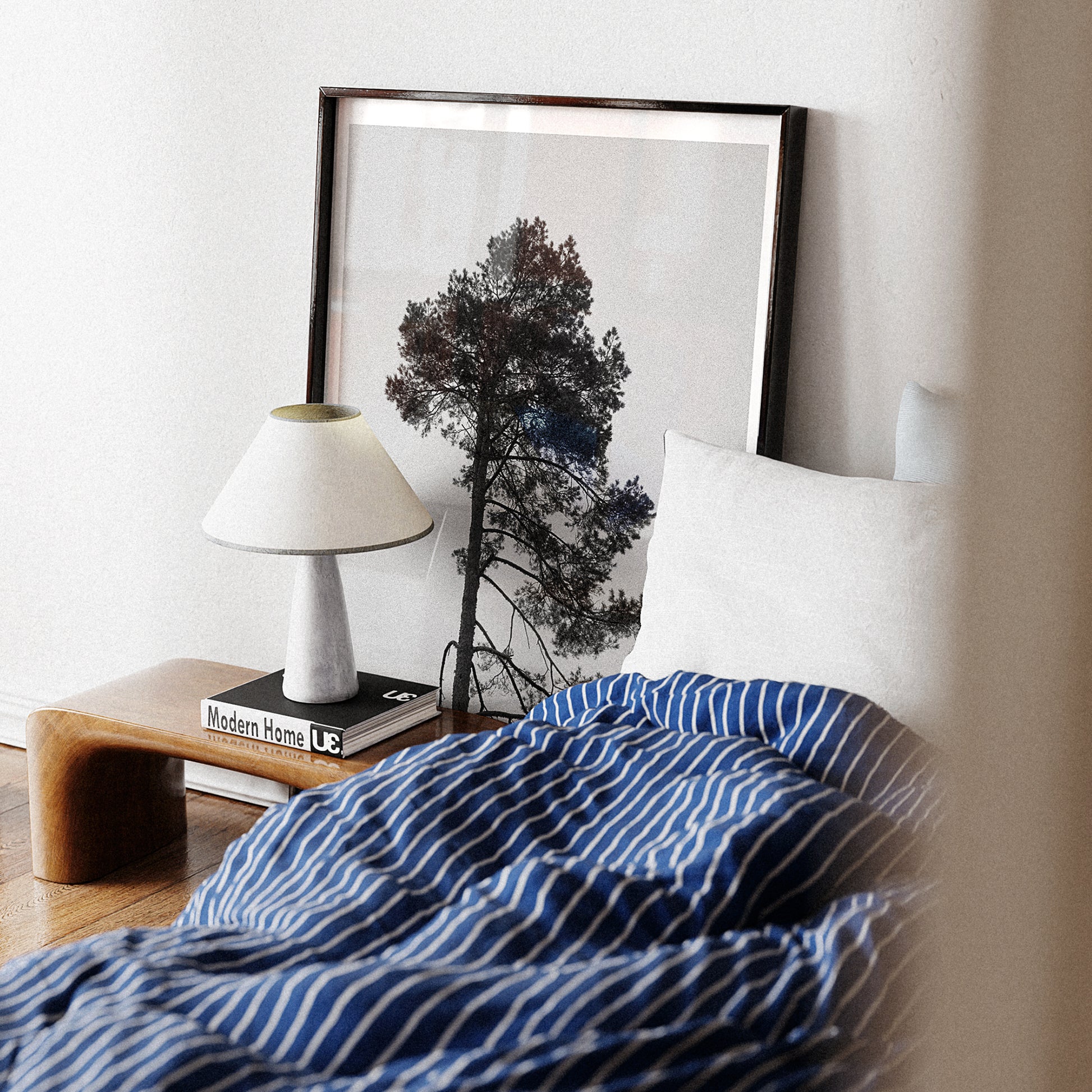 Blue striped blanket on a bed with a lamp and framed picture in the background