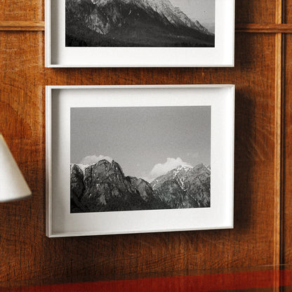 Two framed black and white mountain landscapes on a wooden wall.