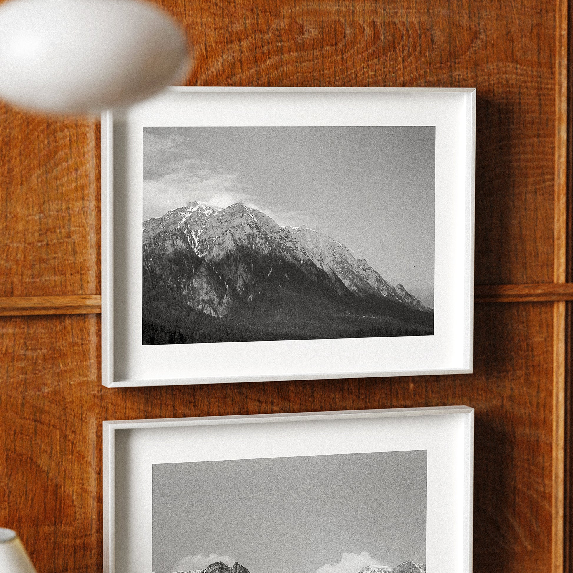 Two framed black and white mountain landscapes on a wooden wall.