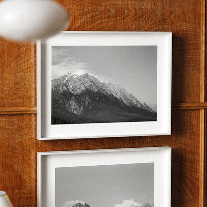 Two framed black and white mountain landscapes on a wooden wall.