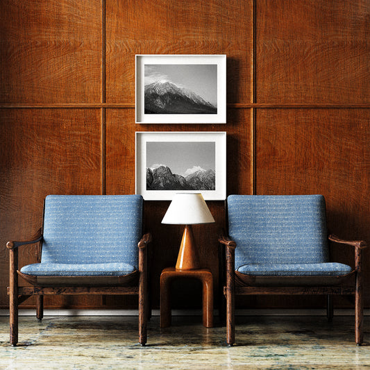 Two blue cushioned chairs in a room with wooden paneling and framed mountain pictures.