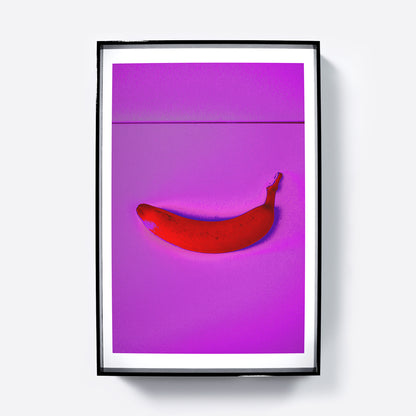 Framed artwork of a red banana on a pink background.