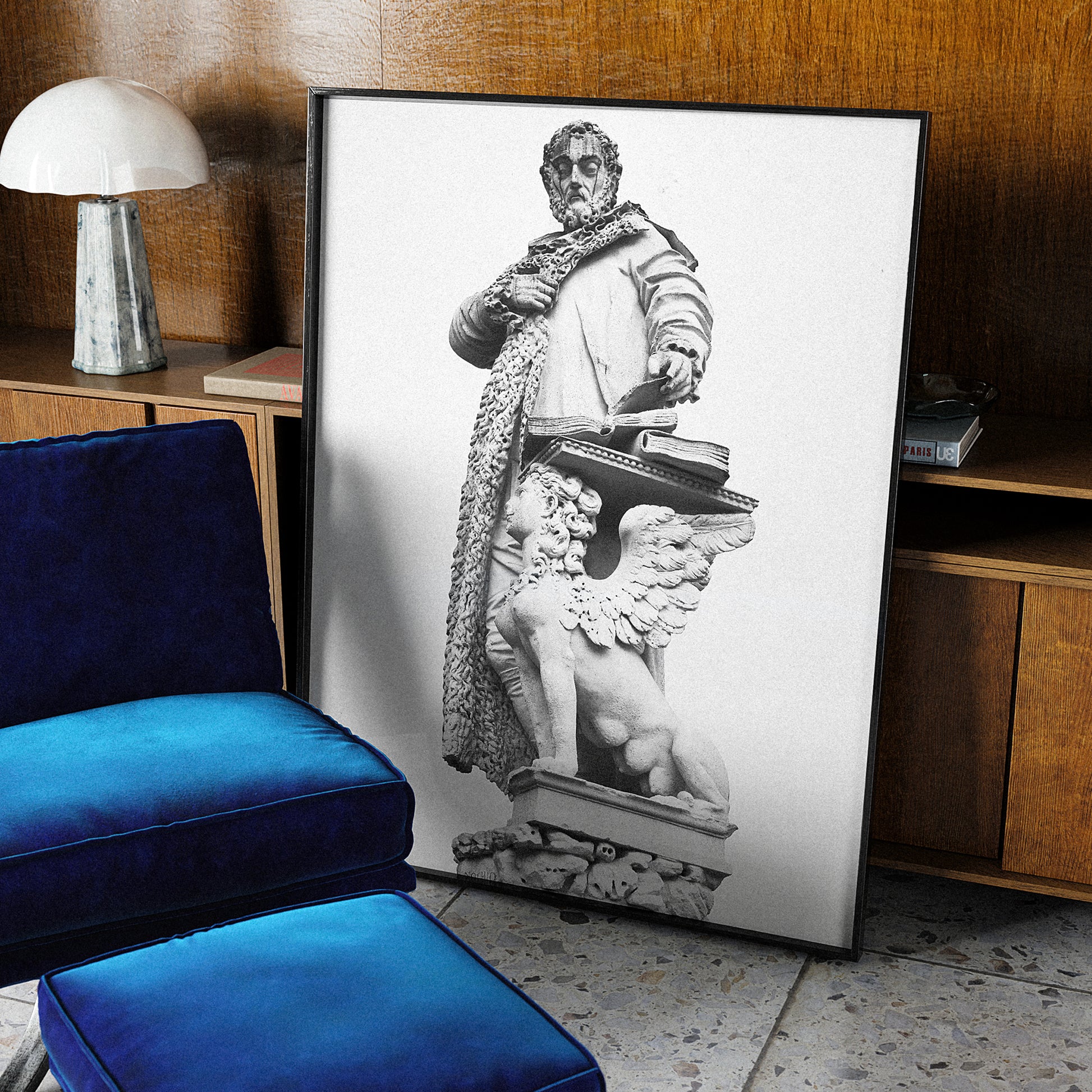 Framed artwork of a classical statue in a room with a blue velvet chair and wooden furniture.